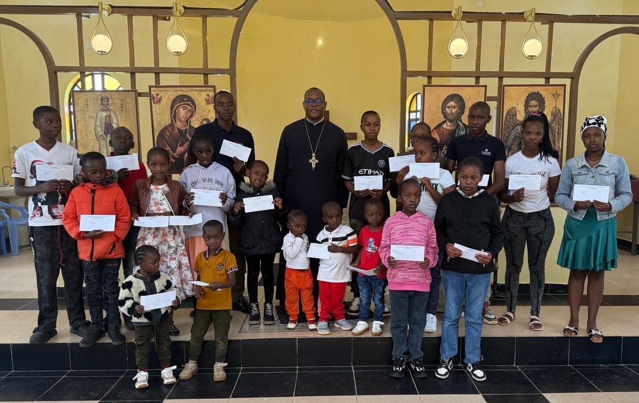 AOA scholarship recipients of all ages standing with Fr Thiani, each holding their award letter.